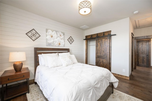 bedroom featuring a barn door, wood finished floors, attic access, and baseboards