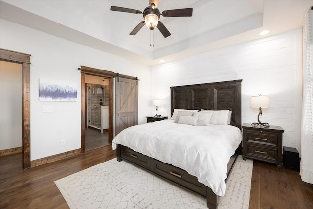 bedroom with a barn door, a raised ceiling, dark wood finished floors, and baseboards