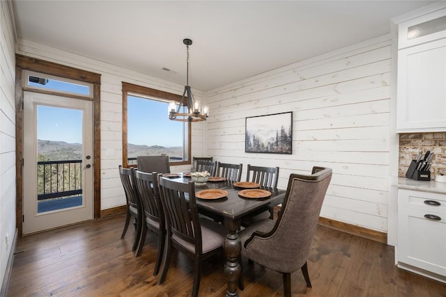 dining room with baseboards, dark wood-type flooring, wood walls, and an inviting chandelier