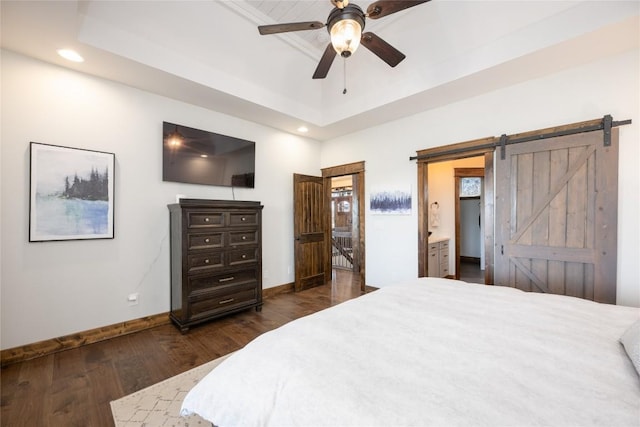 bedroom with a barn door, baseboards, dark wood-style flooring, a tray ceiling, and recessed lighting