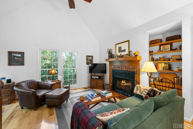 living room with a tiled fireplace, ceiling fan, high vaulted ceiling, and light hardwood / wood-style floors