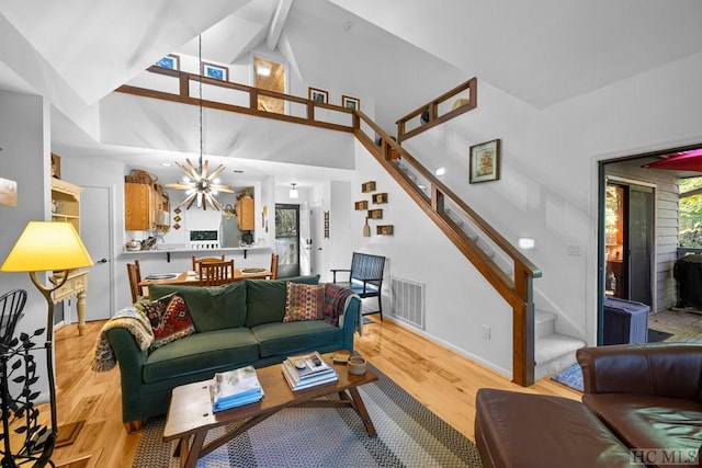 living room featuring beam ceiling, high vaulted ceiling, a chandelier, and light wood-type flooring