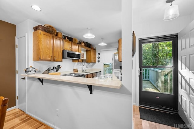 kitchen with a kitchen bar, decorative light fixtures, appliances with stainless steel finishes, kitchen peninsula, and light hardwood / wood-style floors