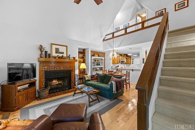 living room featuring ceiling fan, a fireplace, high vaulted ceiling, and light hardwood / wood-style flooring