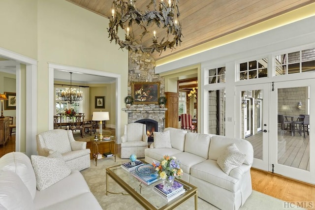 living room with wood ceiling, a towering ceiling, a notable chandelier, a stone fireplace, and french doors