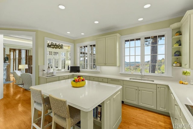 kitchen with sink, crown molding, a kitchen breakfast bar, a kitchen island, and light wood-type flooring