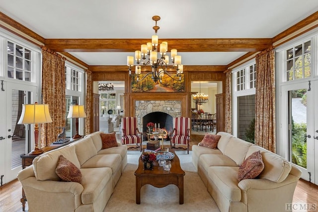 living room featuring beamed ceiling, a stone fireplace, a healthy amount of sunlight, and a notable chandelier