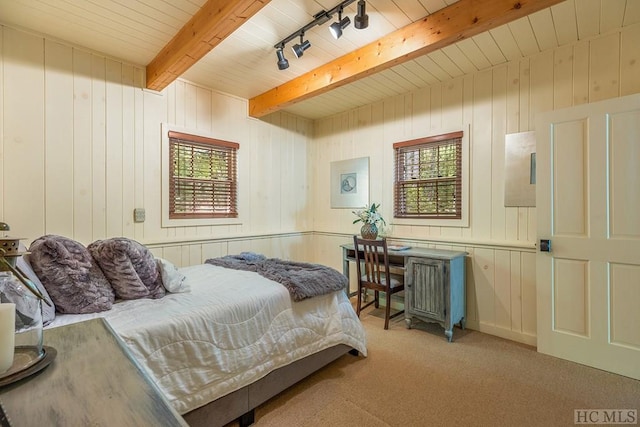 carpeted bedroom featuring wooden walls, rail lighting, and beam ceiling