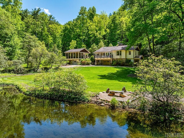 exterior space featuring a sunroom, a deck with water view, and a lawn