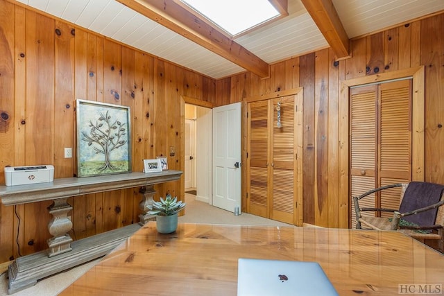 carpeted home office with beamed ceiling, a skylight, and wood walls