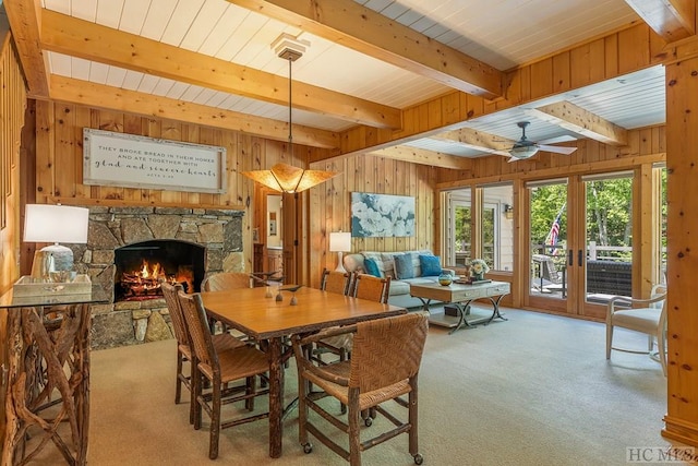 dining room with a stone fireplace, light colored carpet, beam ceiling, and wood walls