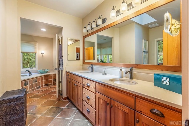 bathroom with tile patterned floors, vanity, tiled bath, and a skylight