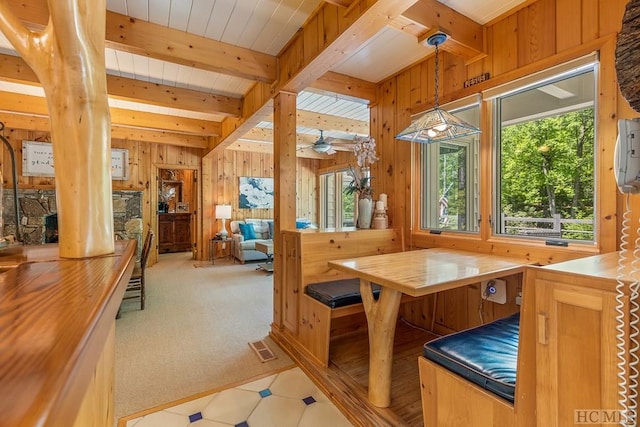 dining room featuring beamed ceiling, light tile patterned flooring, and wood walls