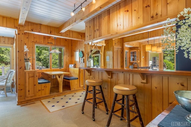 bar featuring wood walls, hanging light fixtures, light colored carpet, track lighting, and beam ceiling