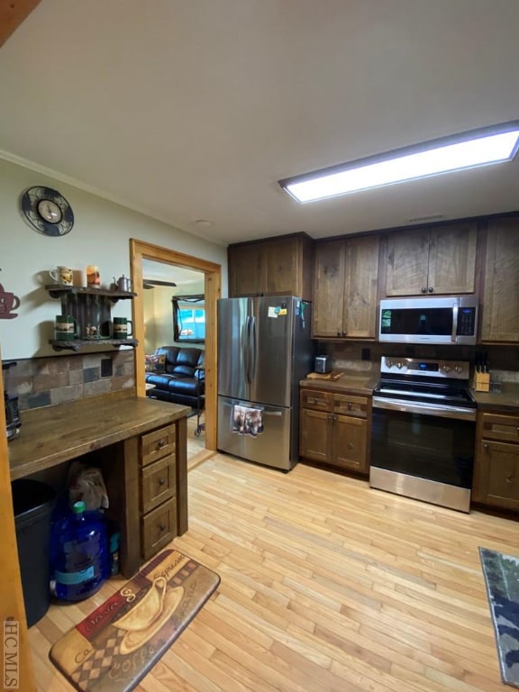 kitchen with ornamental molding, appliances with stainless steel finishes, dark brown cabinetry, and light hardwood / wood-style floors