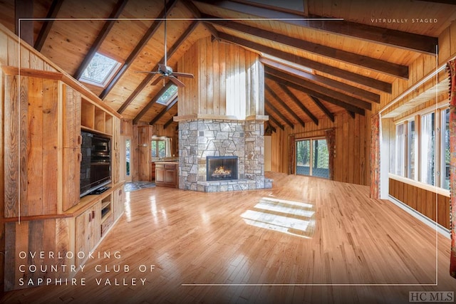 unfurnished living room featuring beam ceiling, wood-type flooring, wooden walls, ceiling fan, and a fireplace