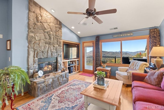 living room with ceiling fan, a stone fireplace, light hardwood / wood-style floors, and vaulted ceiling