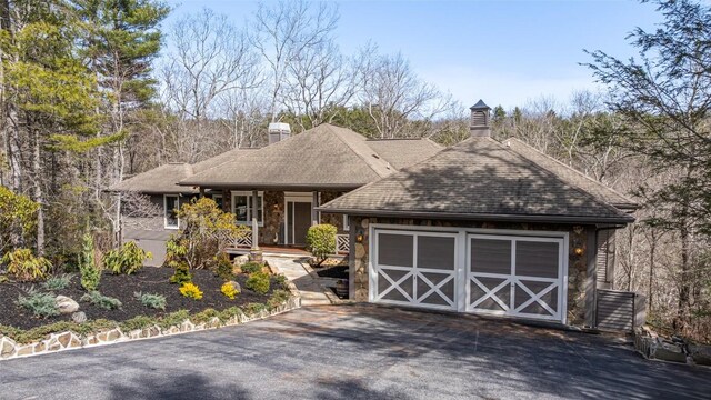 ranch-style house with aphalt driveway, an attached garage, stone siding, and roof with shingles