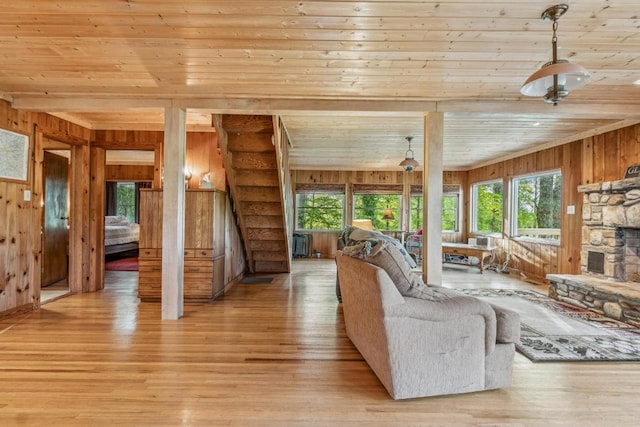 living room featuring wood walls, wood ceiling, light wood-type flooring, and a stone fireplace