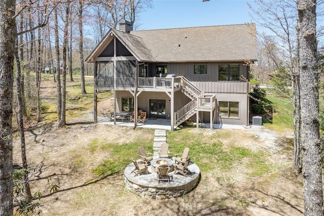 back of house with roof with shingles, stairs, an outdoor fire pit, a chimney, and a patio area