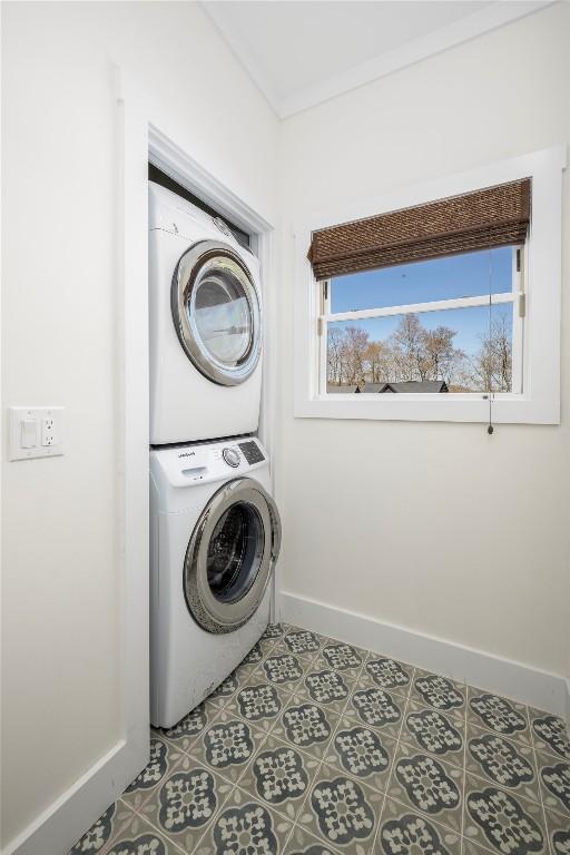 clothes washing area with laundry area, baseboards, and stacked washer and clothes dryer