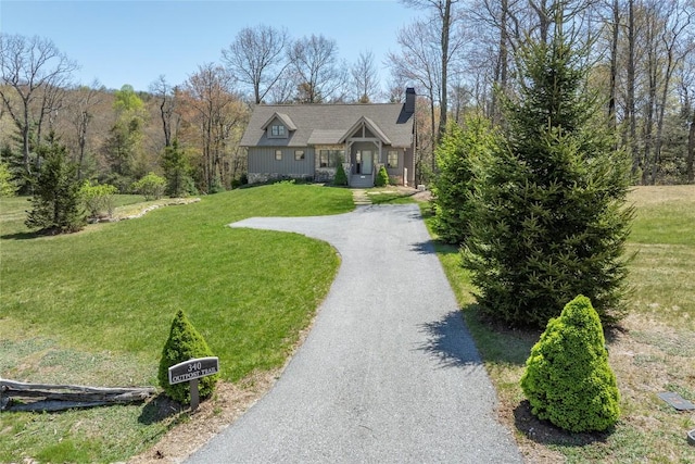 new england style home with a front lawn, driveway, and a chimney