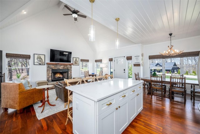 kitchen featuring a stone fireplace, a breakfast bar area, dark wood-type flooring, white cabinets, and ceiling fan with notable chandelier