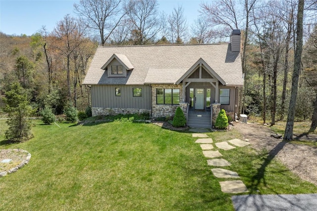 chalet / cabin with board and batten siding, roof with shingles, a front yard, and a chimney