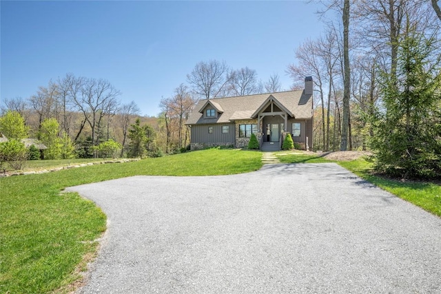 view of front facade featuring board and batten siding, aphalt driveway, a chimney, and a front lawn