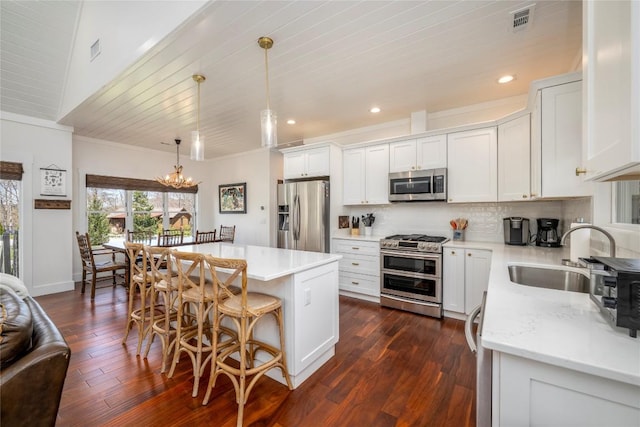 kitchen with a breakfast bar area, backsplash, appliances with stainless steel finishes, a sink, and an inviting chandelier