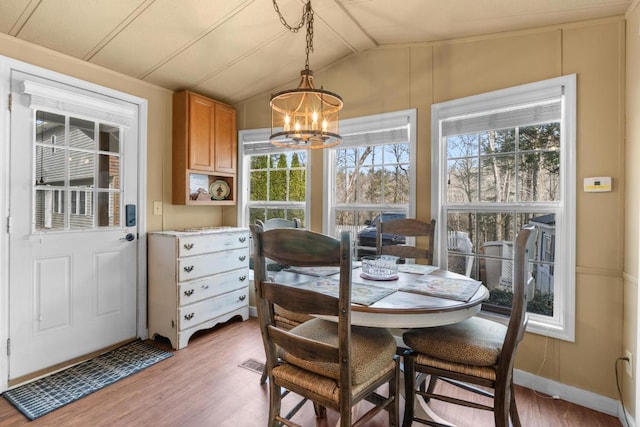 dining area featuring hardwood / wood-style floors, vaulted ceiling, and an inviting chandelier