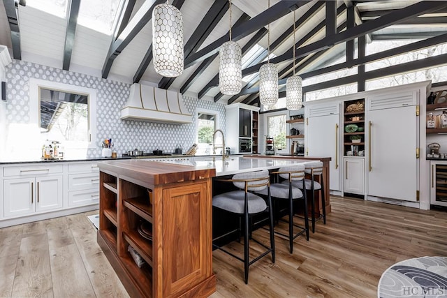 kitchen featuring white cabinetry, an island with sink, custom range hood, and lofted ceiling with beams