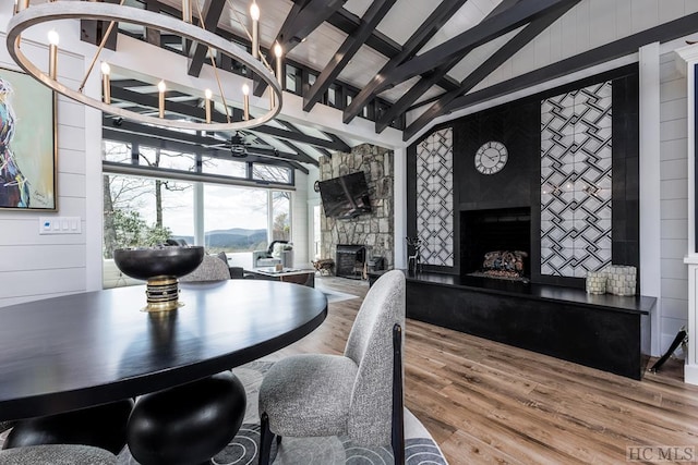 dining space featuring a stone fireplace, hardwood / wood-style floors, high vaulted ceiling, a notable chandelier, and beam ceiling