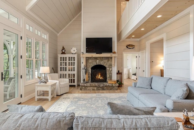 living room featuring light wood-type flooring, wood ceiling, wood walls, a stone fireplace, and high vaulted ceiling