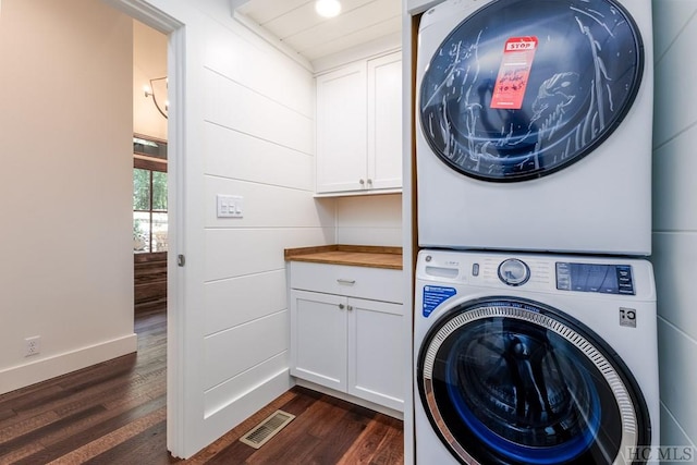 laundry area featuring stacked washer and dryer, dark hardwood / wood-style floors, and cabinets