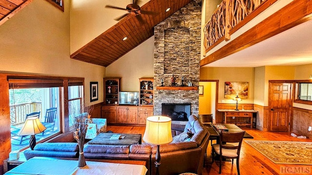 living room with a stone fireplace, light hardwood / wood-style flooring, ceiling fan, and a high ceiling