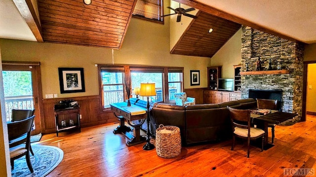 living room featuring wood ceiling, hardwood / wood-style flooring, ceiling fan, high vaulted ceiling, and a stone fireplace