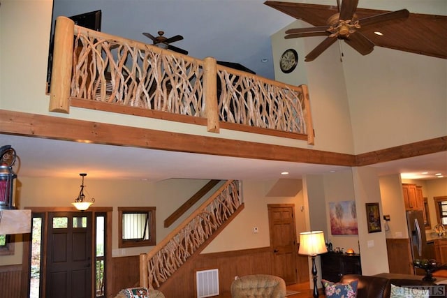 entryway with high vaulted ceiling, ceiling fan, and wood walls