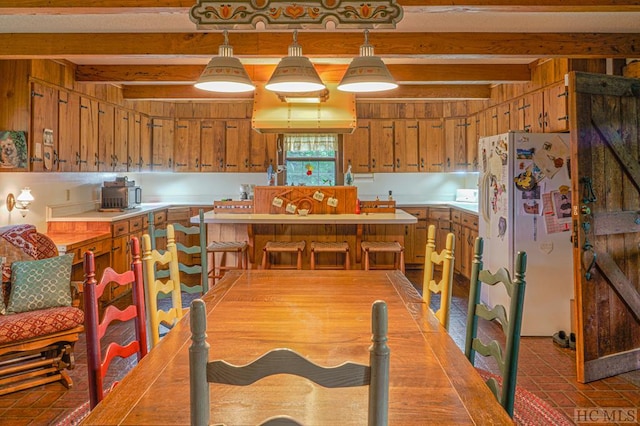 kitchen with beam ceiling, hanging light fixtures, a kitchen bar, and white refrigerator