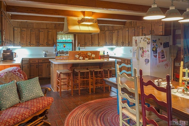 kitchen with beam ceiling, a kitchen island, range hood, white refrigerator with ice dispenser, and a kitchen bar