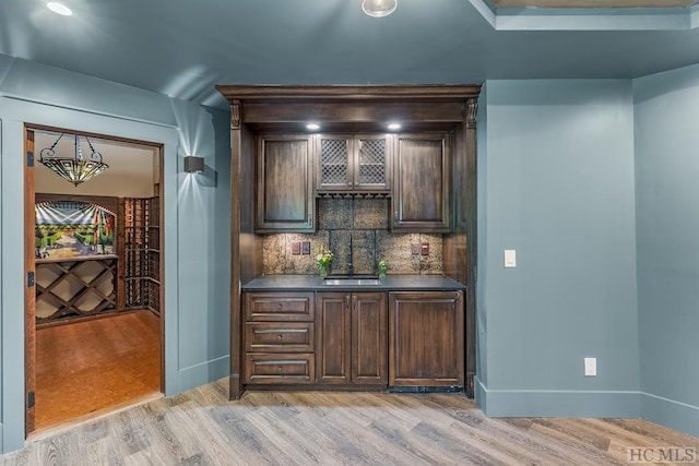 bar featuring tasteful backsplash, sink, dark brown cabinets, and light hardwood / wood-style flooring