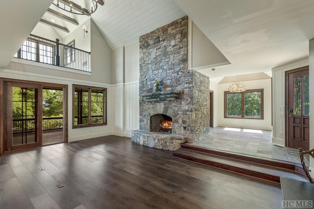 unfurnished living room featuring hardwood / wood-style flooring, beam ceiling, high vaulted ceiling, a notable chandelier, and a fireplace