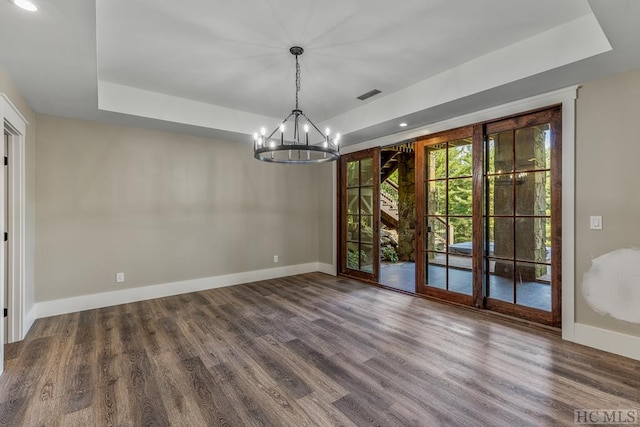 unfurnished dining area featuring dark hardwood / wood-style flooring, a raised ceiling, and a chandelier