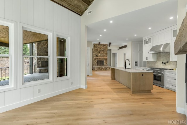 kitchen with exhaust hood, a large island, white cabinets, vaulted ceiling, and stainless steel range