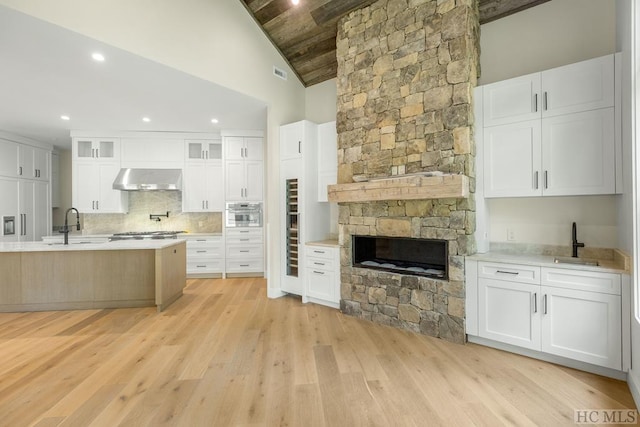 kitchen featuring lofted ceiling, exhaust hood, white cabinetry, tasteful backsplash, and sink