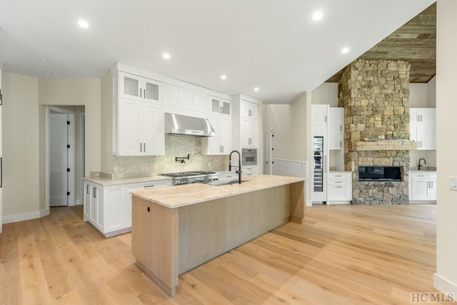 kitchen with exhaust hood, white cabinetry, light hardwood / wood-style floors, sink, and a center island with sink