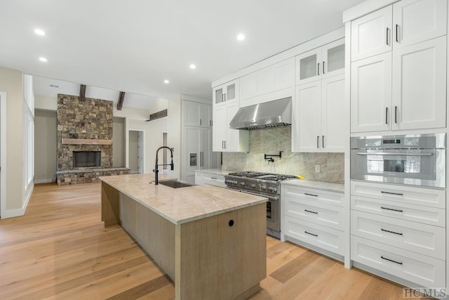 kitchen with wall chimney exhaust hood, sink, white cabinets, a kitchen island with sink, and stainless steel appliances