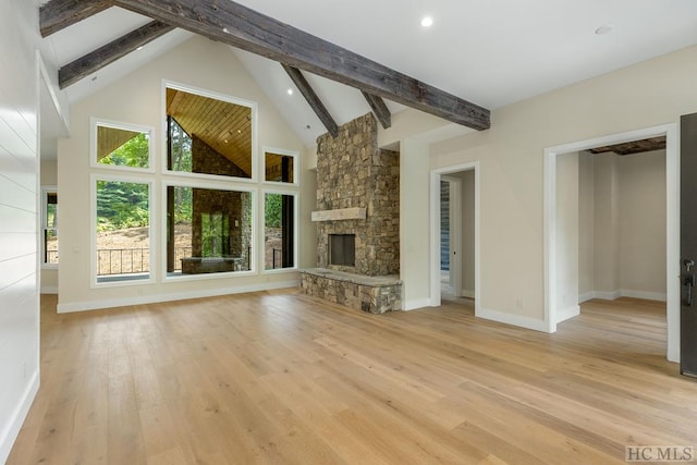 unfurnished living room featuring high vaulted ceiling, beamed ceiling, a stone fireplace, and light wood-type flooring