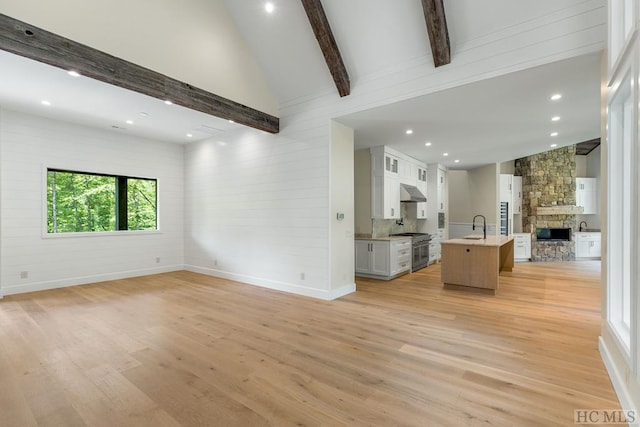 unfurnished living room featuring sink, beam ceiling, a fireplace, high vaulted ceiling, and light hardwood / wood-style floors