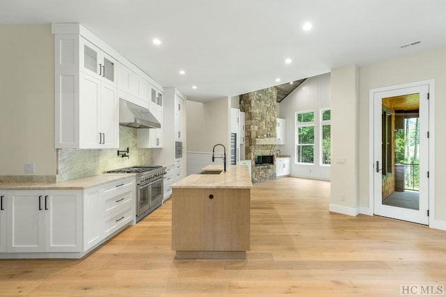 kitchen featuring double oven range, white cabinetry, sink, and an island with sink